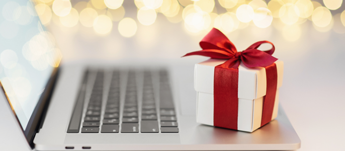 Ein Laptop mit einem Geschenkkarton auf der Tastatur, verziert mit einer roten Schleife.