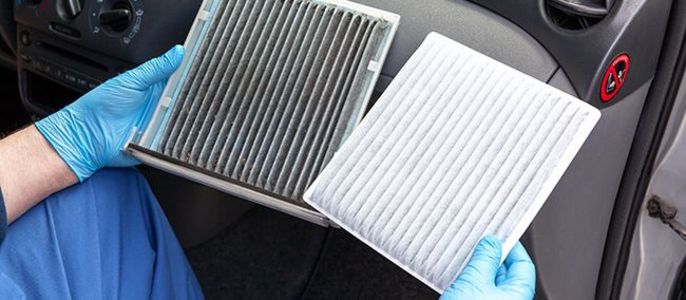 Eine Person mit blauen Handschuhen hält zwei Auto-Luftfilter, einen schmutzigen und einen sauberen.