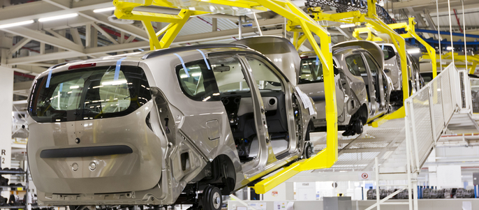 Ein Autofließband in einer Fabrik, bei dem die Fahrzeugrahmen von gelben Förderbändern angehoben und bewegt werden.