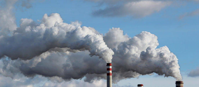 Hohe Schornsteine, die dicken weißen Rauch gegen einen blauen Himmel mit vereinzelten Wolken ausstoßen.