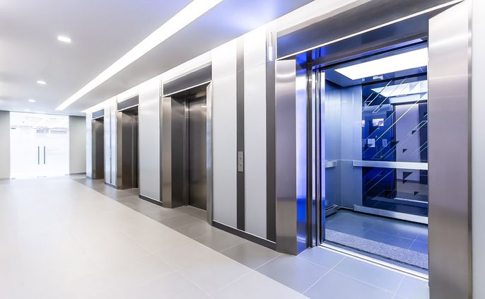 Ein moderner Korridor mit drei Aufzügen, jeder mit einem eleganten Design und einer Glastür, die den Blick ins Innere des Aufzugs freigibt.