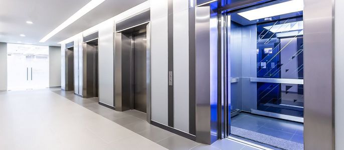 Ein moderner Korridor mit drei Aufzügen, jeder mit einem eleganten Design und einer Glastür, die den Blick ins Innere des Aufzugs freigibt.