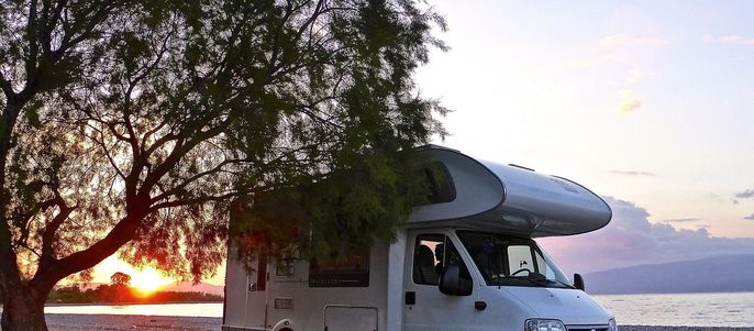 Ein weißes Wohnmobil, das bei Sonnenuntergang unter einem Baum am Strand steht.