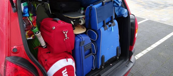 Der Kofferraum eines roten Autos ist mit verschiedenen Gegenständen gefüllt, unter anderem mit Koffern, einem Tennisschläger und einem Skateboard.
