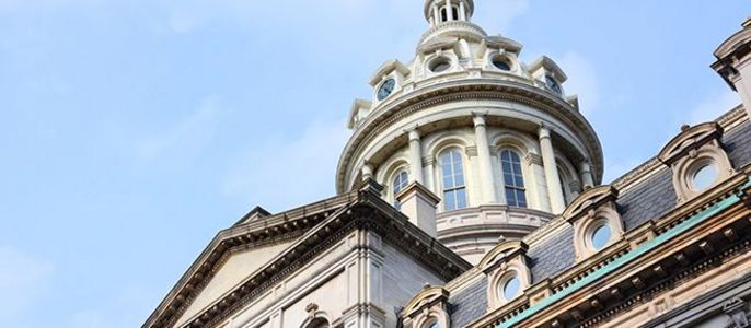 Ein großartiges architektonisches Bauwerk mit einer markanten Kuppel, kunstvollen Details und einer goldenen Turmspitze vor einem klaren blauen Himmel.