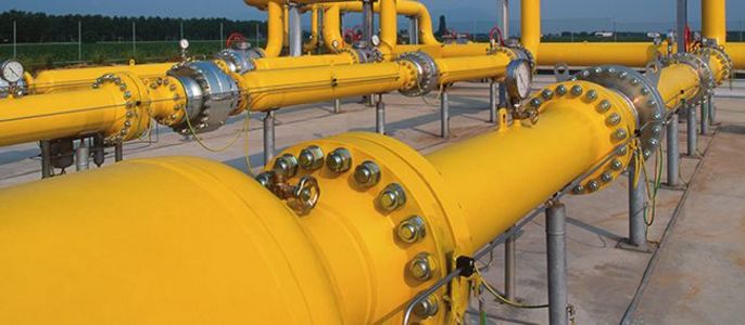 Eine Reihe gelber Rohre, verbunden mit Ventilen und Armaturen, vor einem klaren Himmel und einer grünen Landschaft.