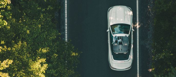 Ein weißes Auto fährt auf einer Straße, die von üppigen grünen Bäumen umgeben ist.