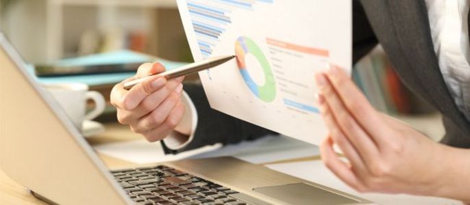 Eine Person im Anzug analysiert ein Balken- und Kreisdiagramm vor einem Laptop.