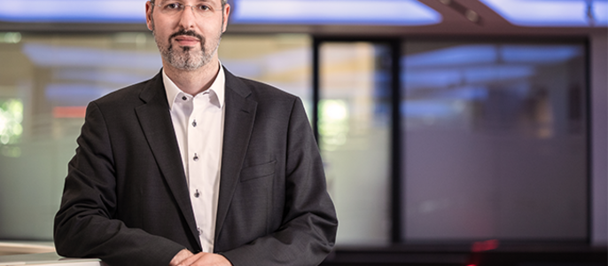 Ein Mann in einem formellen Anzug steht in einem Büro mit moderner Architektur, das von blauen Lichtern beleuchtet wird.