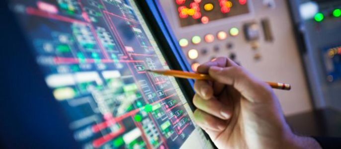 Ein Techniker hält einen Stift in der Hand, um eine Notiz auf einem Computerbildschirm zu machen, der ein komplexes Netz aus miteinander verbundenen Linien und Symbolen anzeigt.