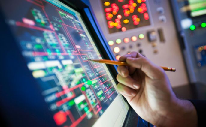 Ein Techniker hält einen Stift in der Hand, um eine Notiz auf einem Computerbildschirm zu machen, der ein komplexes Netz aus miteinander verbundenen Linien und Symbolen anzeigt.