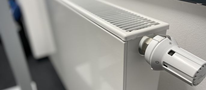 Ein weißer Heizkörper, an dessen Seite ein weißer Thermostat angebracht ist.