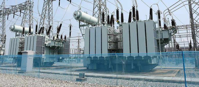 Ein großes Umspannwerk mit mehreren Transformatoren, die durch Stromleitungen verbunden sind, vor einem klaren Himmel.