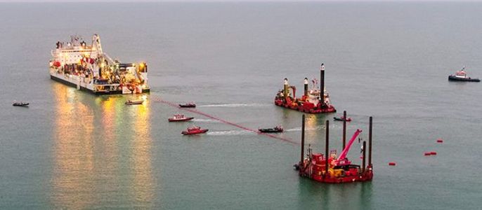 Ein großes Schiff, das im Meer vor Anker liegt, umgeben von kleineren Booten und Plattformen, die alle an einer maritimen Aktivität beteiligt sind.