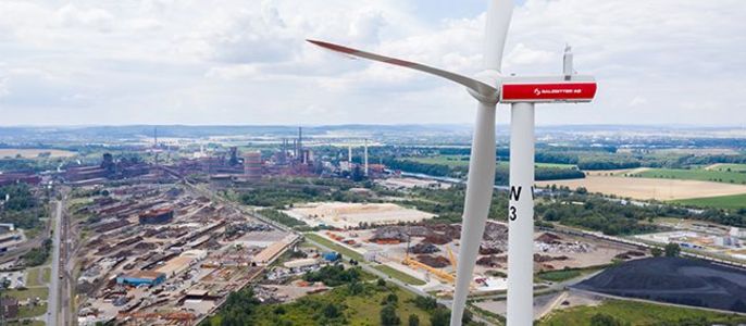 Ein Windrad, die in einem Industriegebiet mit verschiedenen Gebäuden und Infrastrukturen steht.