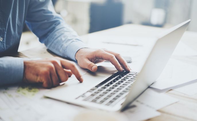 Eine Person, die einen Laptop benutzt und mit den Händen auf der Tastatur tippt.