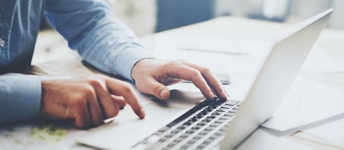 Eine Person, die einen Laptop benutzt und mit den Händen auf der Tastatur tippt.