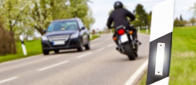 Eine Straße mit einem Motorrad und einem Auto, mit einem weiß-schwarz gestreiften Pfosten an der Seite.