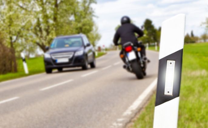 Eine Straße mit einem Motorrad und einem Auto, mit einem weiß-schwarz gestreiften Pfosten an der Seite.