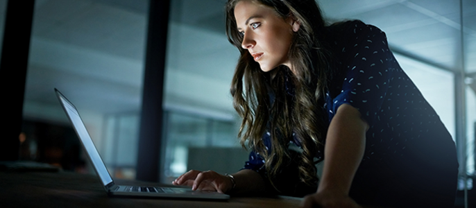 Eine Frau konzentriert sich in einem schwach beleuchteten Raum auf ihren Laptop.