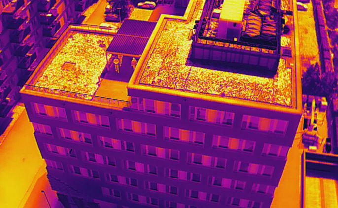 Ein mehrstöckiges Gebäude , umgeben von anderen Gebäuden und Fahrzeugen, aufgenommen mit einer Wärmekamera.