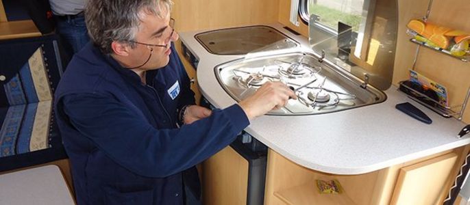 Ein Mann in einer blauen Weste arbeitet an einem Ofen in einem Wohnwagen.