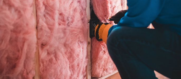 Eine Person in einem blauen Hemd schneidet mit einem gelben Werkzeug durch rosa Isoliermaterial.