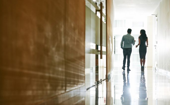 Zwei Personen gehen einen Korridor entlang, an dessen Ende ein helles Licht ist.