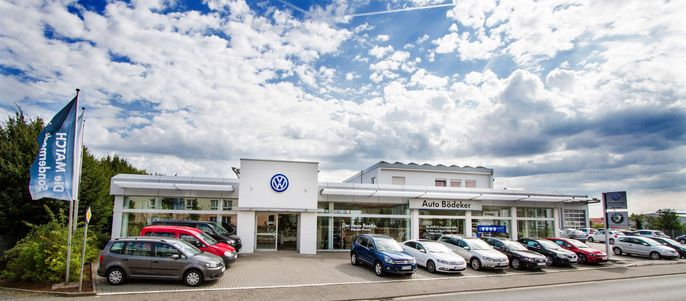 Ein Volkswagen-Autohaus mit mehreren draußen geparkten Autos unter einem blauen Himmel mit vereinzelten Wolken.