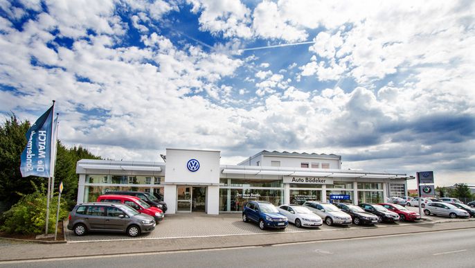 Ein Volkswagen-Autohaus mit mehreren draußen geparkten Autos unter einem blauen Himmel mit vereinzelten Wolken.