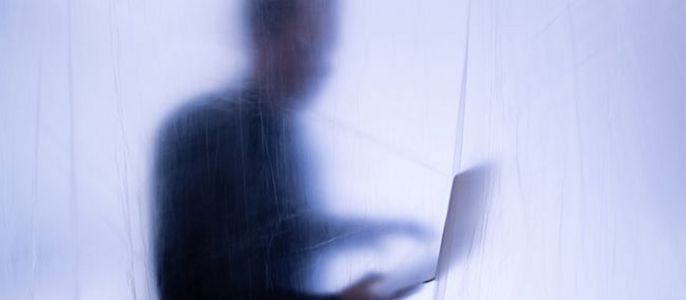 Eine verschwommene Figur einer Person, die einen Laptop hält, umgeben von einem durchscheinenden Material, das eine ätherische und geheimnisvolle Atmosphäre schafft.