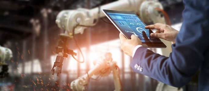 Ein Mann in einem Anzug, der einen Roboterarm mit einem Tablet steuert, während aus dem Ende des Roboters Funken fliegen.