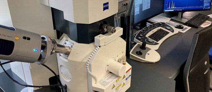 Ein hochentwickeltes wissenschaftliches Instrument mit der Aufschrift "ZEISS" und einem Computerbildschirm, der Daten anzeigt. Die Anlage befindet sich in einem Raum mit einem Fenster, und in der Nähe befinden sich verschiedene Steuertasten und eine Tastatur.