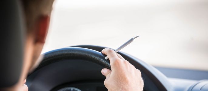 Ein Mann, der ein Auto fährt und einen Stift in der rechten Hand hält, mit einem unscharfen Hintergrund einer Straße.