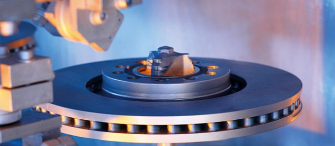 Eine Metallscheibe mit einer zentralen Nabe, die von einer Reihe von kreisförmigen Löchern umgeben ist und an einem mechanischen Arm befestigt ist.