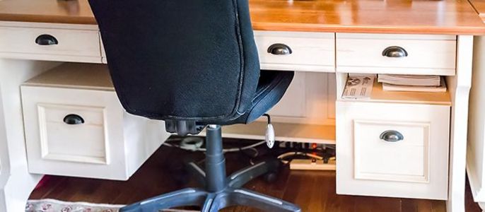 Ein Holzschreibtisch mit einem schwarzen Bürostuhl, einem Computermonitor und diversem Büromaterial.