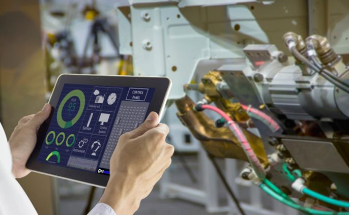 Eine Person hält ein Tablet in der Hand, auf dem verschiedene Daten zu Maschinen angezeigt werden, wobei der Schwerpunkt auf den CO2-Emissionen und den Energieverbrauchsdaten liegt.