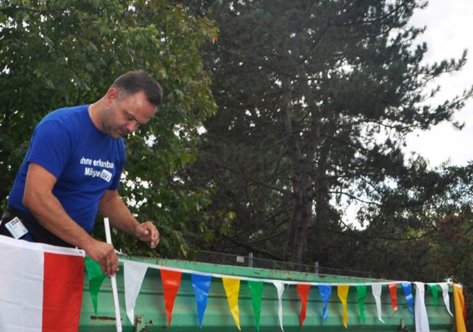 Ein Mann in einem blauen Hemd, der bunte Fahnen an einer grünen Struktur befestigt.