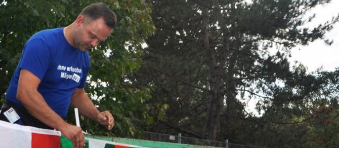 Ein Mann in einem blauen Hemd, der bunte Fahnen an einer grünen Struktur befestigt.