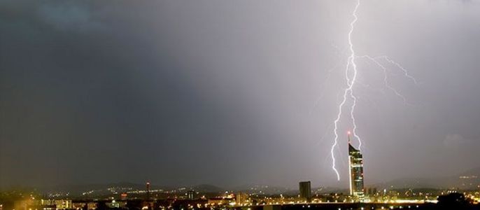 Eine nächtliche Stadtlandschaft mit einem markanten Blitz, der in ein hohes Gebäude einschlägt.