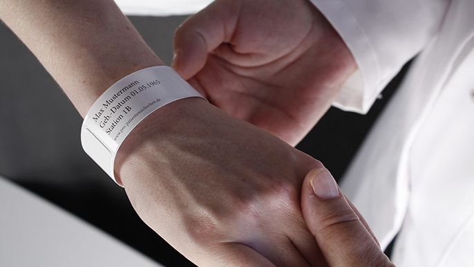 Ein Armband mit Textinformationen, das am Handgelenk einer Person getragen wird.