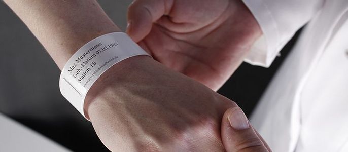 Ein Armband mit Textinformationen, das am Handgelenk einer Person getragen wird.