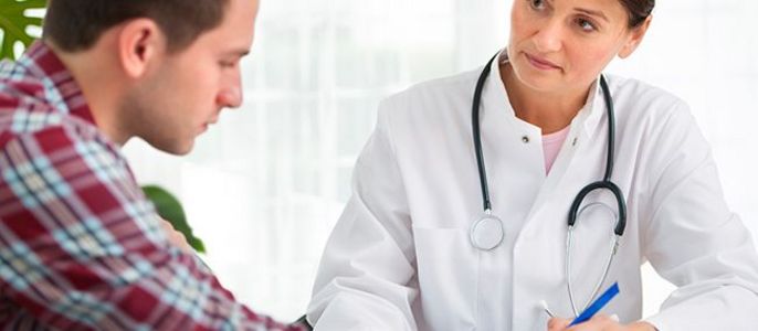Ein medizinisches Fachpersonal, vermutlich ein Arzt, in einer Sprechstunde mit einem Patienten. Der Arzt schreibt etwas auf ein Papier, während der Patient zuschaut.