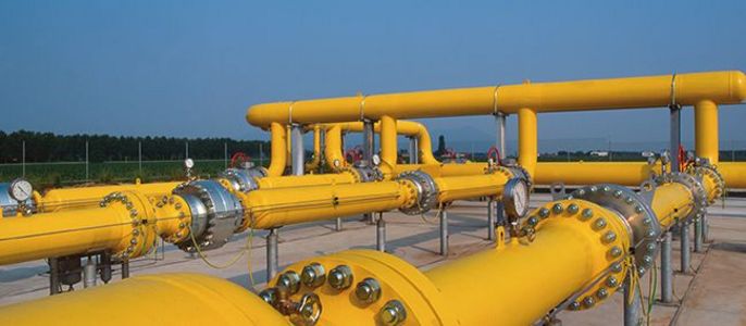 Eine Reihe von gelben Rohren, die mit Ventilen und Armaturen verbunden sind, vor einem klaren blauen Himmel und einer grünen Landschaft.