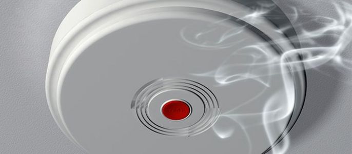 Ein Rauchmelder mit einem roten Knopf, zu dem Rauch aufsteigt.