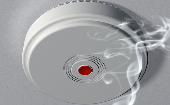 Ein Rauchmelder mit einem roten Knopf, zu dem Rauch aufsteigt.