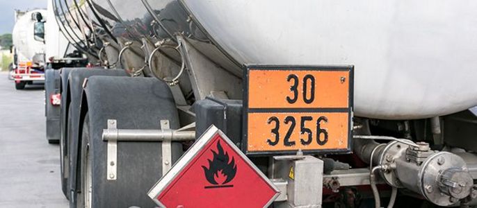 Ein großer Tankwagen mit einem Nummernschild und einem Warnschild, mit einem anderen Tankwagen im Hintergrund.