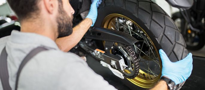 Ein Mann in einer Werkstatt, der aufmerksam das Hinterrad eines Motorrads inspiziert.