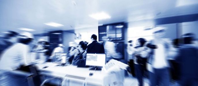 Eine geschäftige Büroumgebung mit Menschen, die sich bewegen, Computern auf Schreibtischen und einem Unschärfeeffekt, der ein Gefühl der Bewegung vermittelt.