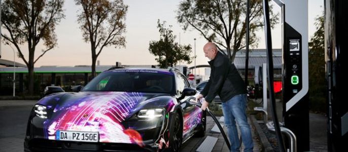 Ein Mann, der ein Elektroauto an einer Ladestation auflädt, wobei das Auto ein lebhaftes kosmisches Design aufweist.